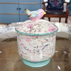 a bird figurine is sitting on top of a glass container that sits on a table