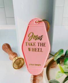 a pink keychain with the words jesus take the wheel on it next to a potted plant