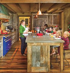 a woman standing in a kitchen next to a table filled with children and an adult