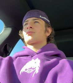 a young man wearing a purple hoodie sitting in a car