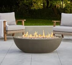 a fire pit sitting on top of a patio next to two chairs and a table