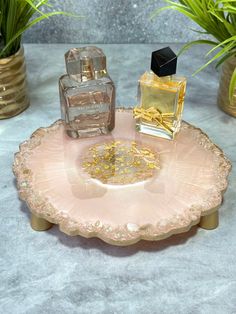 two perfume bottles sitting on top of a pink tray next to some potted plants