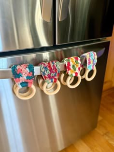 three baby bibs hanging on the handle of a refrigerator door, one is made out of fabric