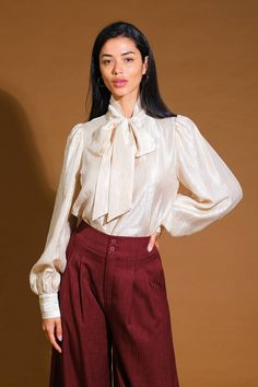 A woven top featuring front bow tie and long blouson sleeve with cuff Details: Self : 34% Tencel 34% Nylon 32% Polyester Size & Fit - Model is 5`8" And Wearing Size Small- Measurements Taken From Size Small- Approx. Length: 23" Fall Puff Sleeve Blouse With Bow, Fall Puff Sleeve Blouse With Bow Detail, Tie Sleeve Tops For Fall Parties, Fall Party Tops With Tie Sleeves, Fall Party Top With Tie Sleeves, Gold Long Sleeve Blouse For Work, Gold Long Sleeve Office Blouse, Classic Long Sleeve Blouse With Bow, Formal Balloon Sleeve Tops For Fall