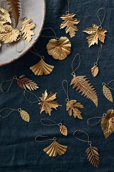 gold leaf ornaments are on a blue cloth next to a bowl with leaves hanging from it