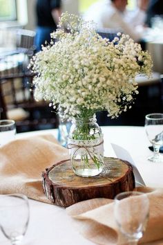 a vase filled with baby's breath sitting on top of a wooden slice at a table