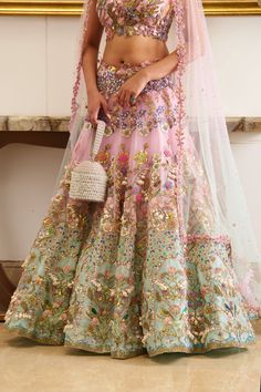 A 3-piece bridal lehenga set in pastel pink and blue, embroidered with botanical motifs and embellished with precious crystals, beads, mirror, sequins, and sea-shell detailing, creates an absolutely modern regal look. Evoking a summer and princess vibe, the set features a floor-length lehenga skirt adorned with floral embroidery, detailed with sea-shell detailing and sparks of crystals and beads. This look is completed with a shaded tulle blue and pink dupatta. Cap-sleeved designer blouse with sweetheart neckline embellished with botanical motifs. The blouse contains a left side open metal zip. The flowy translucent dupatta drenched in a pink and blue hue. Floor-length skirt adorned with hand embroidery crafting the flower motifs with the use of sea-shells, crystals, beads, and sequins. Le Multicolor Embellished Lehenga For Wedding, Embellished Multicolor Lehenga For Wedding, Embellished Multicolor Embroidered Sharara For Designer Wear, Designer Multicolor Hand Embellished Choli, Designer Hand Embellished Multicolor Choli, Multicolor Hand Embellished Designer Choli, Multicolor Hand Embellished Dress For Reception, Hand Embellished Multicolor Dress For Reception, Multicolor Hand Embellished Lehenga For Reception