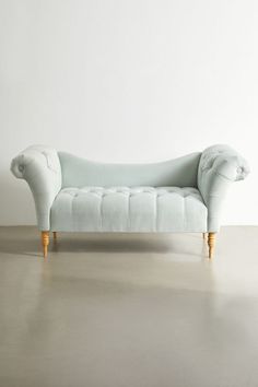 an upholstered chaise lounger in light blue velvet with wooden legs and feet