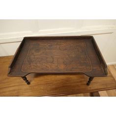 an old wooden tray with carvings on the bottom and legs, sitting on a wood floor