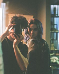 a man and woman are standing in front of a mirror taking pictures with their cell phones