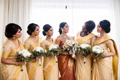 a group of women standing next to each other in front of a window holding bouquets