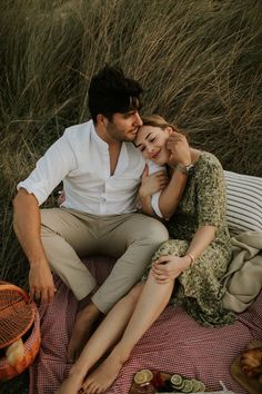 a man and woman sitting on top of a blanket next to each other