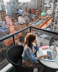 a woman sitting at a table with a laptop on her lap looking out over the city