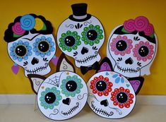 four sugar skulls with colorful flowers on them are sitting in front of a yellow wall