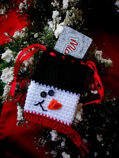 a crocheted snowman ornament hanging from a christmas tree with red ribbon