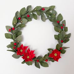 a christmas wreath with poinsettis and greenery on the bottom is displayed against a white wall