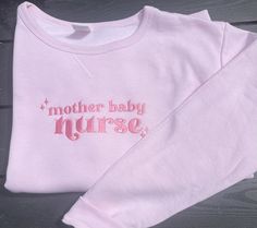 a pink sweatshirt with the words mother baby nurse printed on it, sitting on a wooden surface