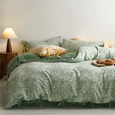 a bed with green comforters and pillows in a white room next to a lamp