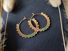 a pair of gold and green beaded hoop earrings on top of a black surface