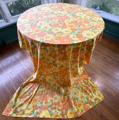 an orange and yellow floral tablecloth on a wooden floor in front of a window