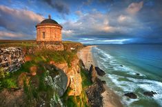 an old building sitting on top of a cliff next to the ocean under a cloudy sky