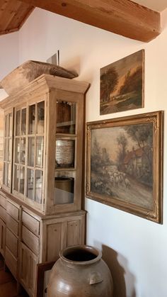 an old china cabinet with paintings on the wall