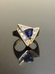 DeKara Designs Clearance Metal- 14K Yellow Gold, .583. 15.6 Grams. Stones- 1 Trillion Cut Ceylon Blue Sapphire 0.85 Carats, 21 Tapered Baguette Diamonds G-H Color VS2 Clarity 0.90 Carats. Size- Ring is a 6. FREE SIZING Art Deco Inspired Handmade 14K Yellow Gold Ceylon Blue Sapphire Diamond Ring. This ring is inspired by the Art Deco era with unique Trillion Cut Ceylon Blue Sapphire that is set in between three V prongs. There are 21 professionally channel set tapered baguette diamonds surroundin Trillion Cut Sapphire Ring With Diamond For Formal Occasions, Trillion Cut Yellow Gold Rings For Formal Occasions, Trillion Cut Tanzanite Ring For Anniversary, Blue Tanzanite Ring With Trillion Cut, Tanzanite Trillion Cut Ring For Anniversary, Gia Certified Blue Art Deco Jewelry, Blue Art Deco Jewelry Gia Certified, Blue Trillion Cut Ring Fine Jewelry, Blue Trillion Cut Fine Jewelry Ring