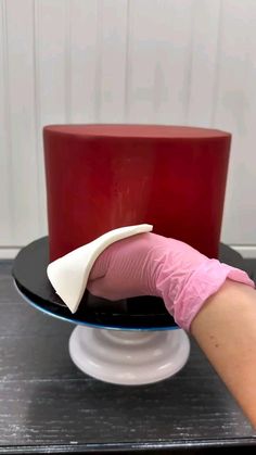 a woman's hand in pink gloves on top of a black and white cake