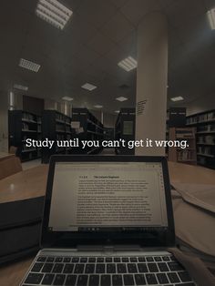 an open laptop computer sitting on top of a wooden table next to a book shelf