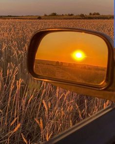 the sun is setting over a wheat field as seen through a rear view mirror on a vehicle