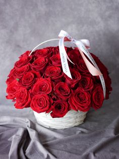 a white basket filled with red roses on top of a gray cloth covered tablecloth