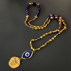 Good Luck Evil Eye and Hamsa Necklace, is a stunning fusion of cultural symbolism and elegant design. This captivating necklace is meticulously crafted, featuring a combination of gold-colored hematite stone beads, blue crystal beads, a sterling silver Hamsa pendant plated with 18k gold, and an 18k gold-plated evil eye glass pendant. At the heart of the necklace lies a sterling silver Hamsa pendant, plated with 18k gold. The Hamsa symbolizes protection and blessings in many cultures, serving as Symbolic Necklaces For Meditation And Festivals, Festive Gemstone Beads Spiritual Jewelry, Gold Necklaces With Colorful Beads As Gifts, Gold Necklaces With Colorful Beads For Gifts, Beaded Jewelry For Meditation And Festivals, Gold Necklace With Gemstone Beads For Festive Occasions, Festive Spiritual Beaded Jewelry, Hand-strung Beaded Necklaces As Festival Gifts, Gold Jewelry With 108 Round Beads