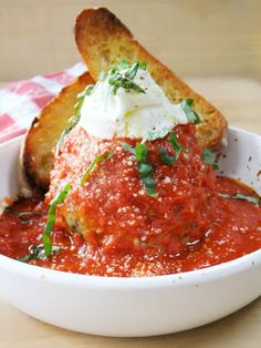 a white bowl filled with meatballs covered in marinara sauce and sour cream cheese