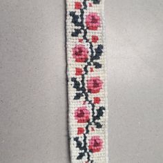 a white and black beaded bracelet with red flowers on the side, sitting on a gray surface