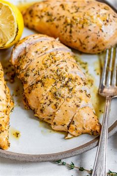 two pieces of chicken on a plate with lemons and herbs next to the whole chicken