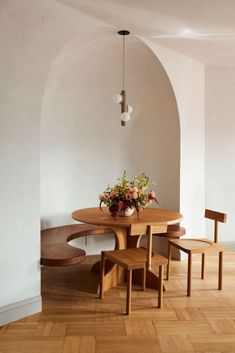 a wooden table with four chairs and a vase on it in a white walled room