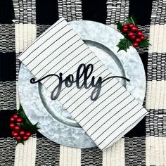 a white plate topped with a paper napkin and holly decoration on top of a black and white checkered table cloth