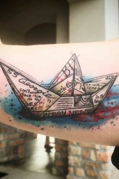 a man's arm with an origami boat tattoo on it