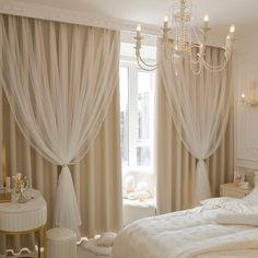 a white bedroom with chandelier and curtains