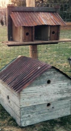 a bird house sitting on the ground next to a pole with two birds in it