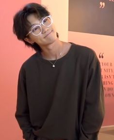 a young man wearing glasses standing in front of a pink wall with writing on it