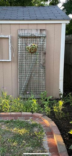 a small shed with a gate and flowers in the garden next to it, on a brick path