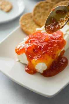 a spoon with some food on it is being drizzled over crackers