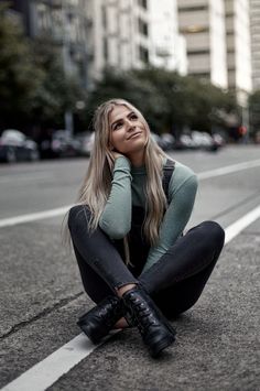 a woman sitting on the side of a road next to a street with tall buildings