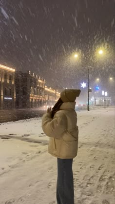 a woman standing in the snow at night with her back to the camera looking up