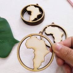 a hand holding a wooden ornament with the shape of africa in front of it