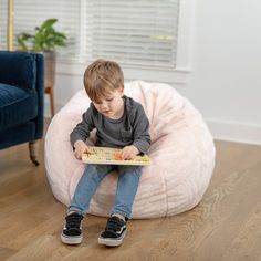 a young boy sitting on a bean bag chair reading a book in his living room