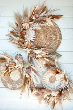 three woven baskets with dried flowers and leaves hanging from the side of a white wall