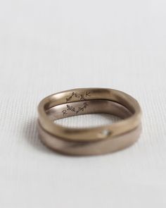 two gold wedding bands with birds engraved on the side, sitting on a white surface