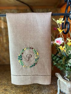 a towel hanging on a rack next to flowers and a vase with an embroidered monogram